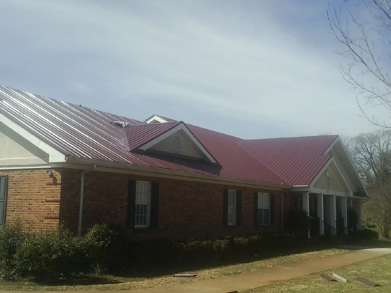 Red metal roof with gabled entries on a long brick building, from a Hail Damage Roof Repair job in Martins Ferry