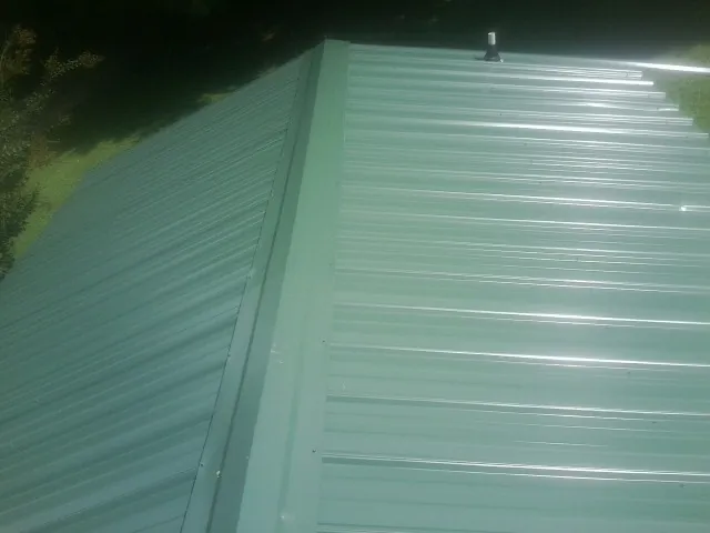 New green metal panels meeting at the ridge of a roof — Flat Roof Repair work by our crew in Martins Ferry