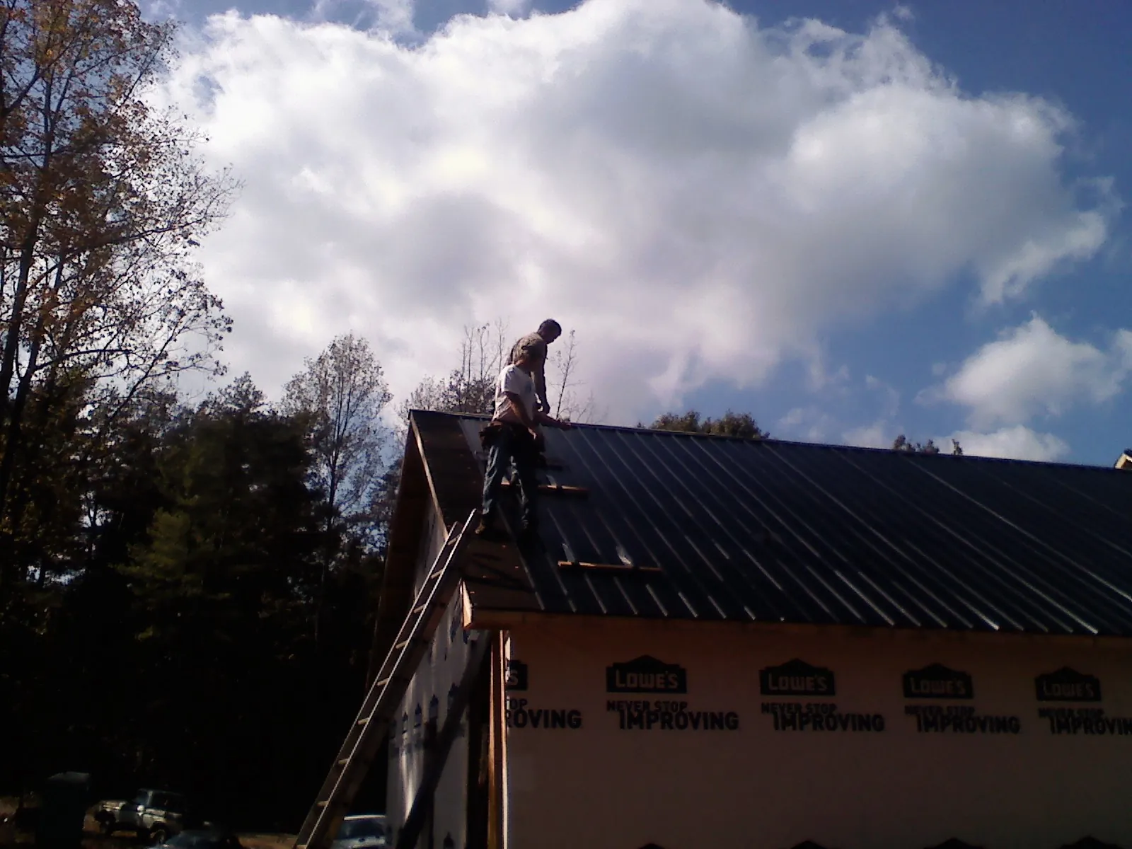 Roofer fastening dark metal panels high against a cloudy sky, from a Roof Inspection job in Martins Ferry