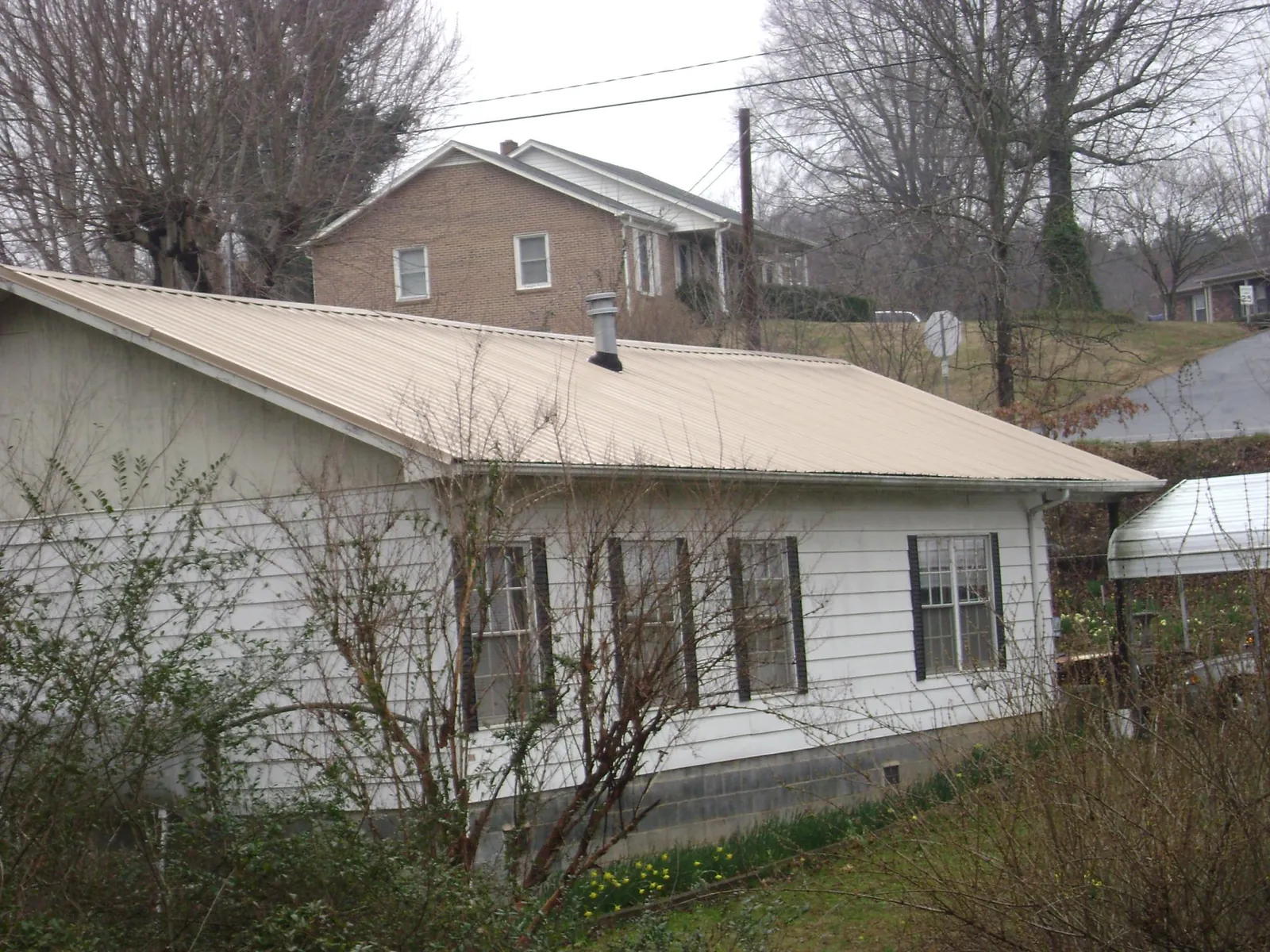 Tan metal roof on a white sided house set into a hillside — Commercial Roofing by Roofing Brothers in Martins Ferry