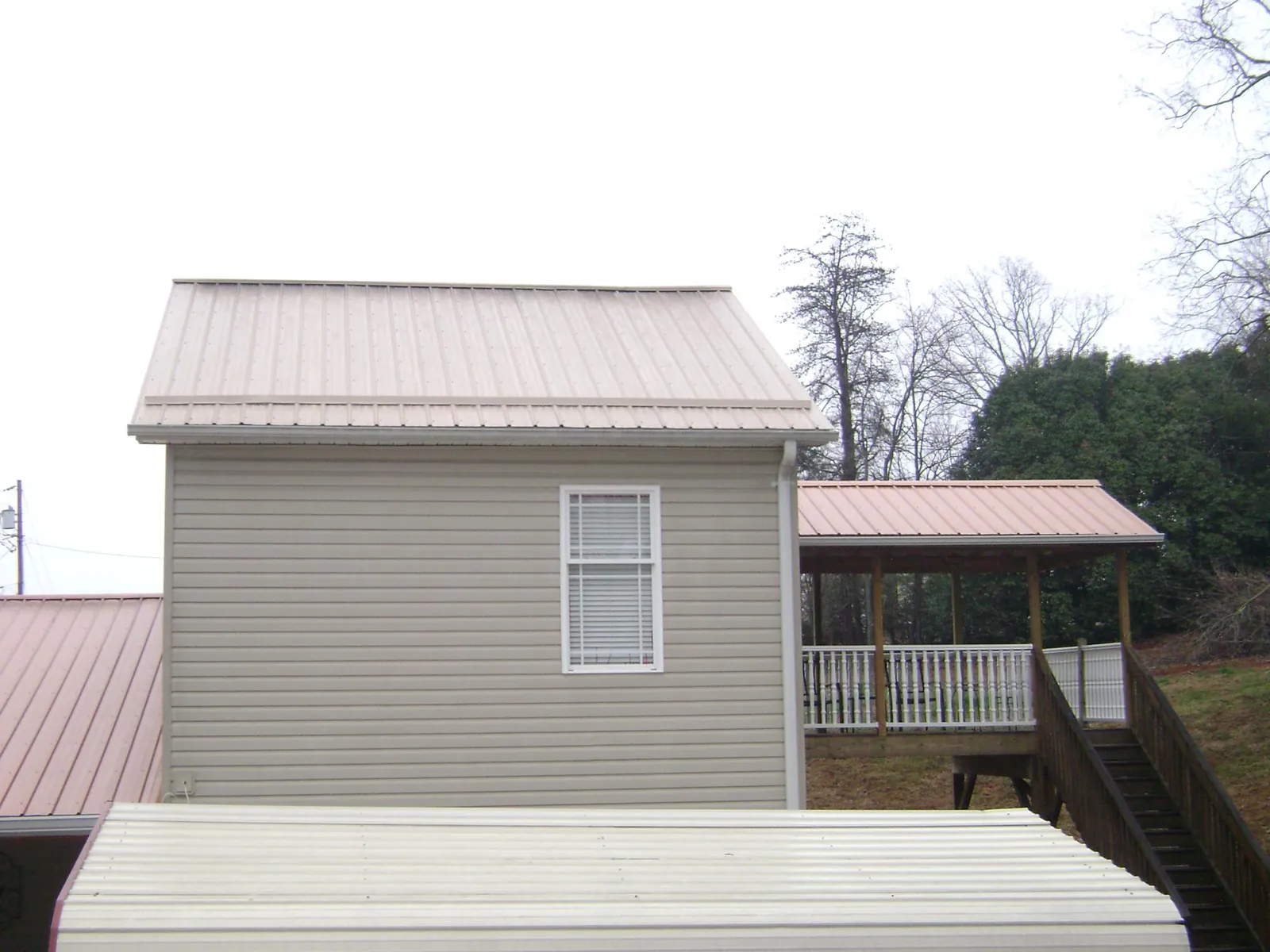 Tan metal roofs on a two story addition and attached porch, from a Roof Replacement job in Martins Ferry